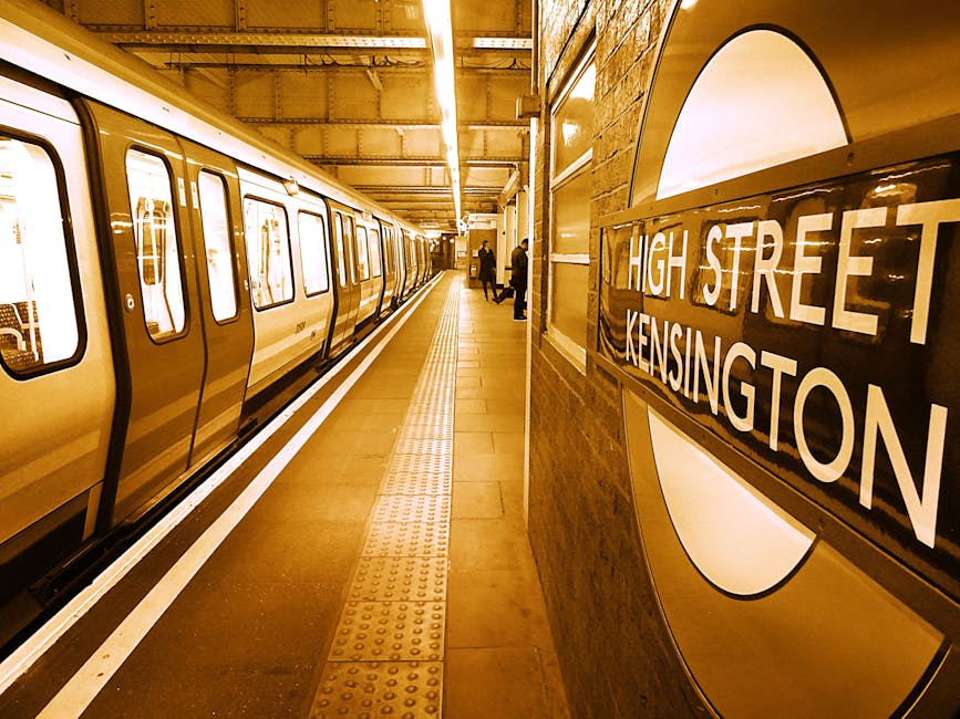 A rectangular metal street sign mounted on a brick wall, welcoming visitors to South Kensington with the text 'Welcome to South Kensington SW7' in black and red lettering on a white background. The si